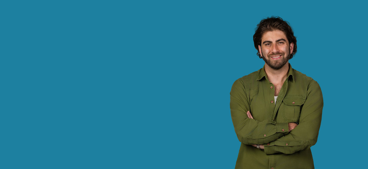 Person standing with arms crossed against a blue background.