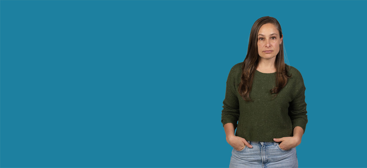 Person with hands in pockets against a blue background